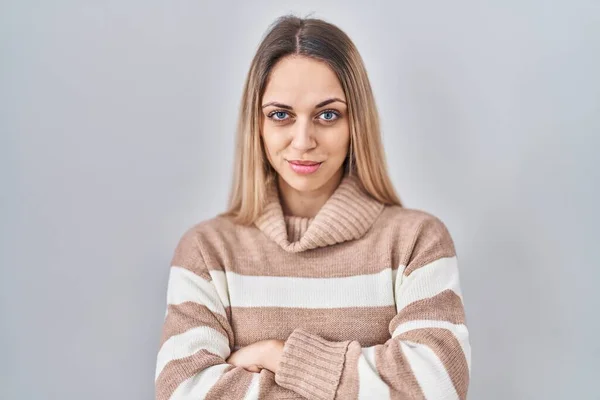 Young blonde woman wearing turtleneck sweater over isolated background skeptic and nervous, disapproving expression on face with crossed arms. negative person.