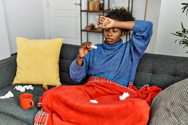 Stock image African american woman holding thermometer sitting on sofa at home