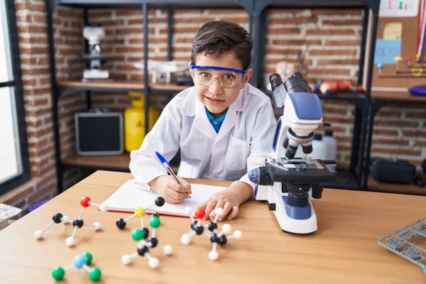 Adorable Hispanic Boy Student Using Microscope Writing Notebook Laboratory Classroom — Φωτογραφία Αρχείου