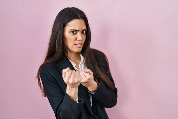Young brunette woman wearing business style over pink background ready to fight with fist defense gesture, angry and upset face, afraid of problem