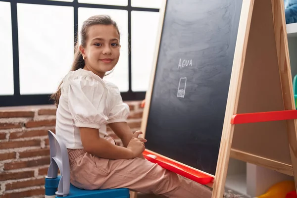 可爱的惊慌失措的女生带着自信的笑容在教室的黑板上画画 — 图库照片