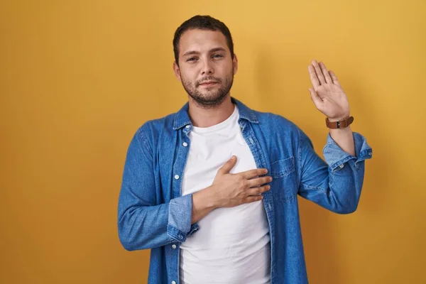 Hispanic Man Standing Yellow Background Swearing Hand Chest Open Palm —  Fotos de Stock