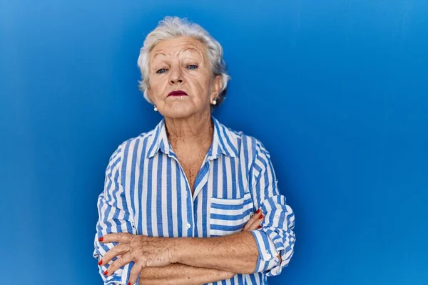 头发灰白的老妇人站在蓝色的背景上 疑神疑鬼 神经质 双手交叉 脸上不悦的表情 消极的人 — 图库照片