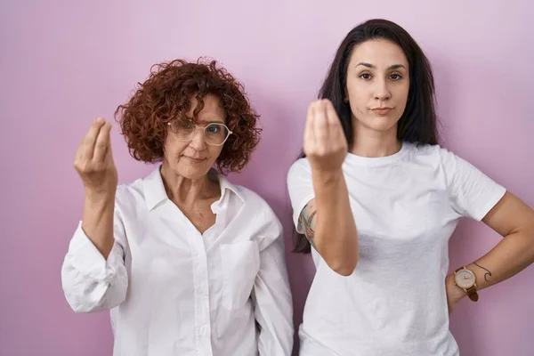 西班牙裔母亲和女儿穿着宽松的白色T恤 背景粉红 手指手画脚地做着意大利式的手势 — 图库照片