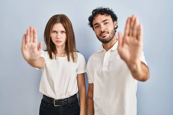 Young couple wearing casual clothes standing together doing stop sing with palm of the hand. warning expression with negative and serious gesture on the face.
