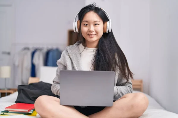 Young chinese woman listening to music sitting on bed at bedroom