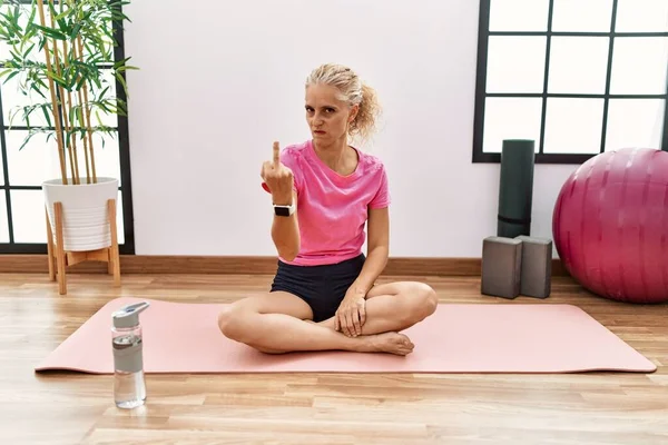 Middle Age Blonde Woman Sitting Yoga Mat Showing Middle Finger — Stock Photo, Image