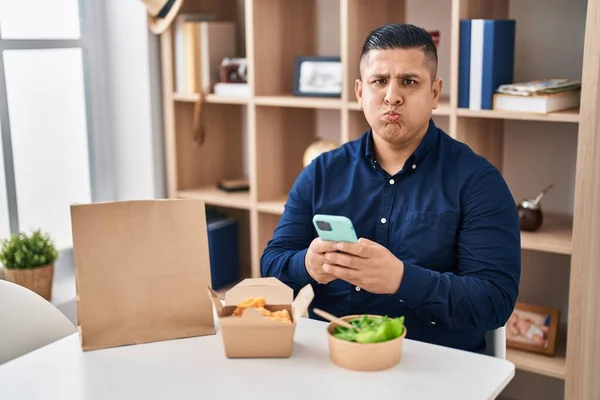 Hispanic Young Man Eating Take Away Food Using Smartphone Puffing —  Fotos de Stock
