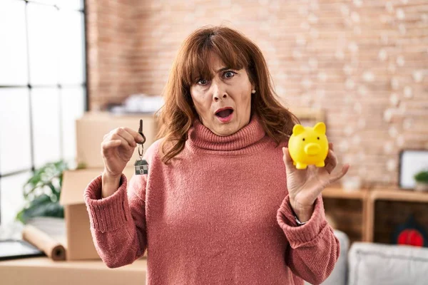 Middle Age Hispanic Woman Holding Piggy Bank House Keys Shock — Stockfoto