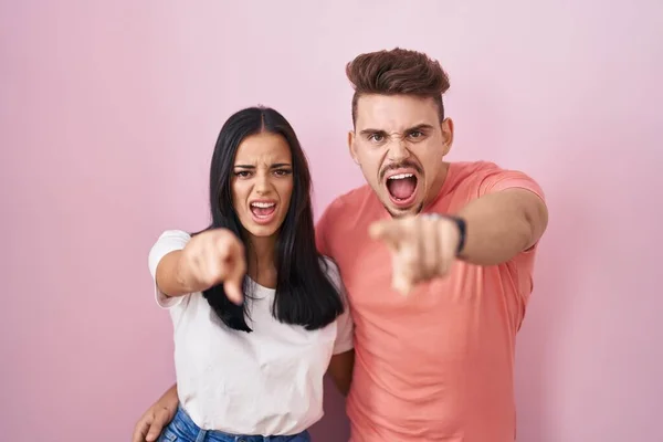 Young Hispanic Couple Standing Pink Background Pointing Displeased Frustrated Camera — стоковое фото