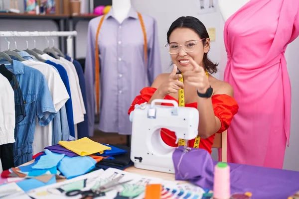 Hispanic young woman dressmaker designer using sewing machine pointing fingers to camera with happy and funny face. good energy and vibes.