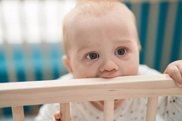 可愛いですCaucasian赤ん坊立っていますオンクレイドルBiting木製Balustradeでベッドルーム — ストック写真