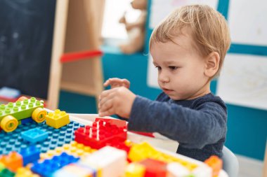 Anaokulundaki masada oturan sevimli sarışın çocuk inşaat bloklarıyla oynuyor.
