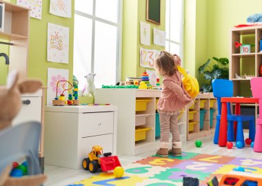 Adorable blonde girl wearing backpack standing at kindergarten
