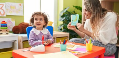 Teacher and toddler sitting on table having language lesson at kindergarten