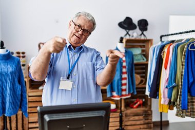 Senior man with grey hair working as manager at retail boutique pointing fingers to camera with happy and funny face. good energy and vibes. 