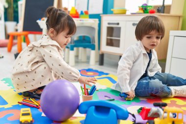 Two kids playing with toys sitting on floor at kindergarten
