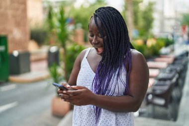 Afro-Amerikalı bir kadın kahve dükkanının terasında akıllı telefon kullanarak gülümsüyor.