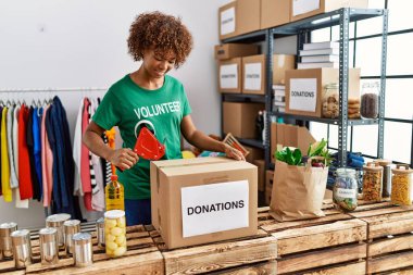 Gönüllü üniforma giyen genç Afrikalı Amerikalı kadın yardım merkezinde bağış kutusu paketliyor.