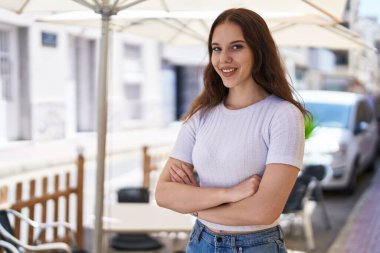 Kendine güvenen genç bir kadın caddede kollarını kavuşturmuş duruyor.