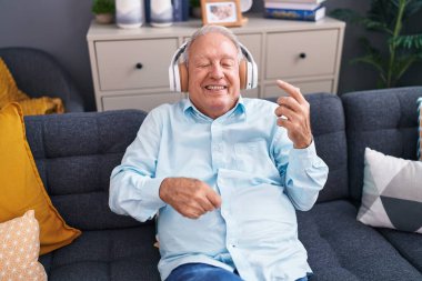 Middle age grey-haired man listening to music doing guitar gesture at home
