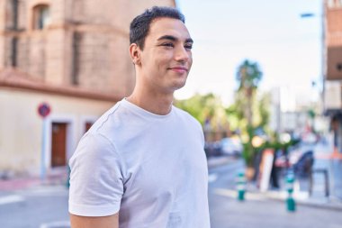 Young hispanic man smiling confident looking to the side at street