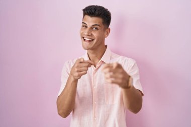 Young hispanic man standing over pink background pointing fingers to camera with happy and funny face. good energy and vibes. 