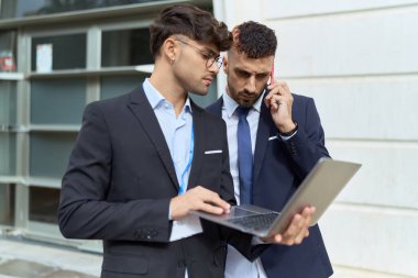 İki İspanyol iş adamı laptoplarını sokakta akıllı telefondan konuşuyorlar.