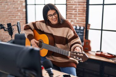 Young hispanic woman musician playing spanish guitar at music studio