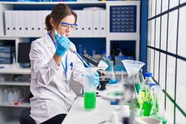 Genç ve güzel İspanyol bilim kadını laboratuarda test tüpüne sıvı döküyor.