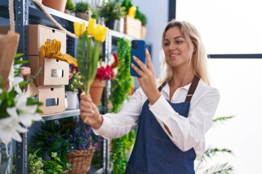 Young blonde woman florist make photo to flowers by smartphone at florist