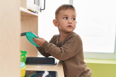 Adorable hispanic boy playing with play kitchen standing at kindergarten