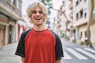 Sokakta kendine güvenen genç sarışın adam gülümsüyor.