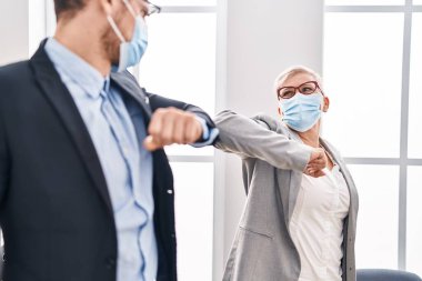 Mother and son business workers wearing medical mask make elbow greeting at office