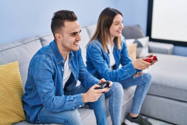 Man and woman couple playing video game sitting on sofa at home