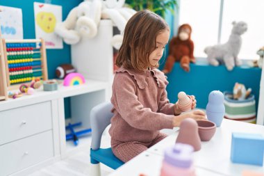 Adorable hispanic girl playing with toys sitting on table at kindergarten