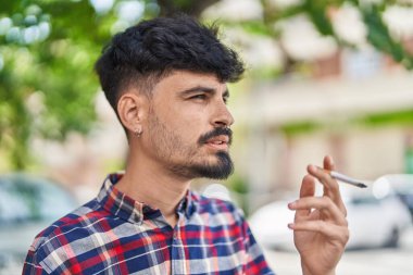 Young hispanic man smoking at street
