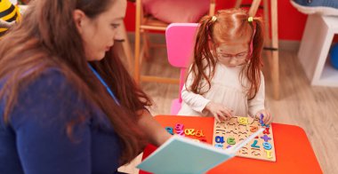 Teacher and student playing with maths puzzle game reading book at kindergarten