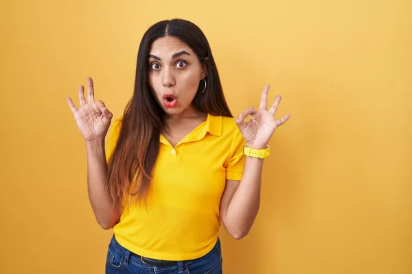 黄色の背景の上に立っている若いアラブの女性は驚きと指でOk承認シンボルをやってショックを受けました クレイジーな表現 — ストック写真