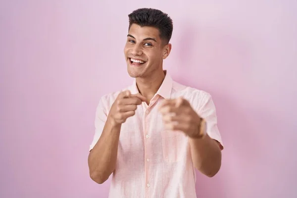 ピンクの背景に立っている若いヒスパニック系の男が幸せと面白い顔でカメラに指を指している 良いエネルギーと振動は — ストック写真
