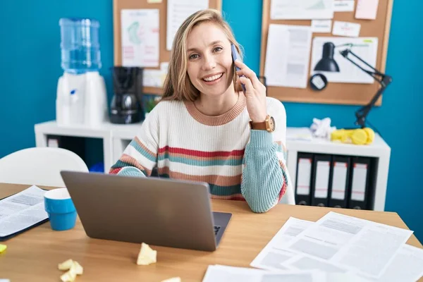 Genç Sarışın Kadını Bilgisayarını Kullanarak Ofiste Akıllı Telefondan Konuşuyor — Stok fotoğraf