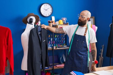 Young bald man tailor holding jacket at clothing factory