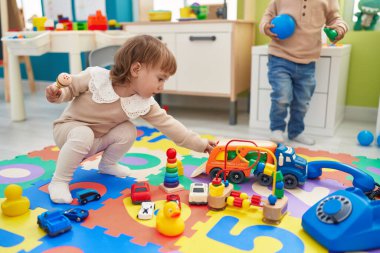 Two kids playing with cars toy sitting on floor at kindergarten