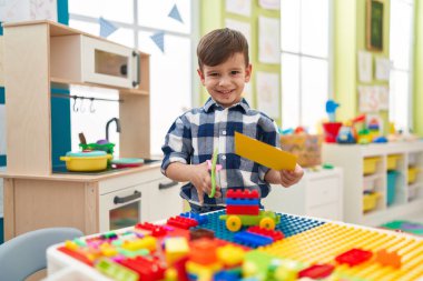 Adorable hispanic boy student smiling confident cutting paper at kindergarten