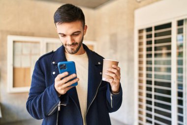 Genç İspanyol adam akıllı telefon kullanıyor, sokakta kahve içiyor.