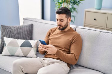 Evdeki kanepede oturan, akıllı telefon kullanan genç bir İspanyol.