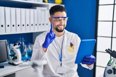 Young handsome man working at scientist laboratory doing online call smiling with an idea or question pointing finger with happy face, number one 