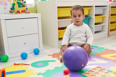 Anaokulunda rahat bir ifadeyle yerde oturan sevimli İspanyol çocuk.