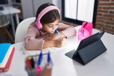 Adorable hispanic girl student sitting on table studying at classroom