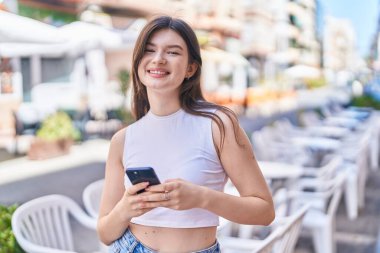 Beyaz bir kadın sokakta akıllı telefon kullanarak gülümsüyor.